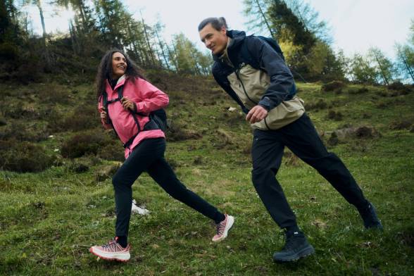 A couple dressed in sporty hiking gear are walking across a clearing
